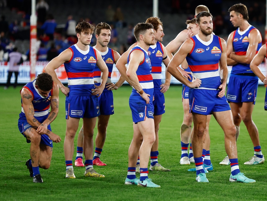 Disappointed Western Bulldogs players react after a loss, with the player on the left almost down on one knee.