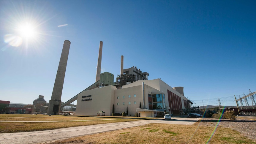 A wide-angle photo of a disused power station, with large white buildings and smokestacks.
