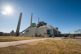 A wide-angle photo of a disused power station, with large white buildings and smokestacks.