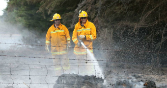 Two CFA firefighters use a hose to put out embers on a farm.