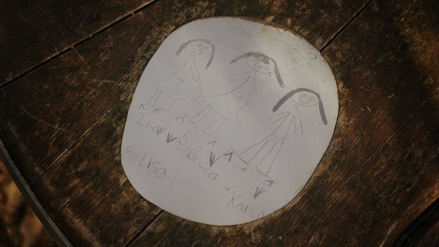 A child's drawing of three girls which is embedded in a wooden bench
