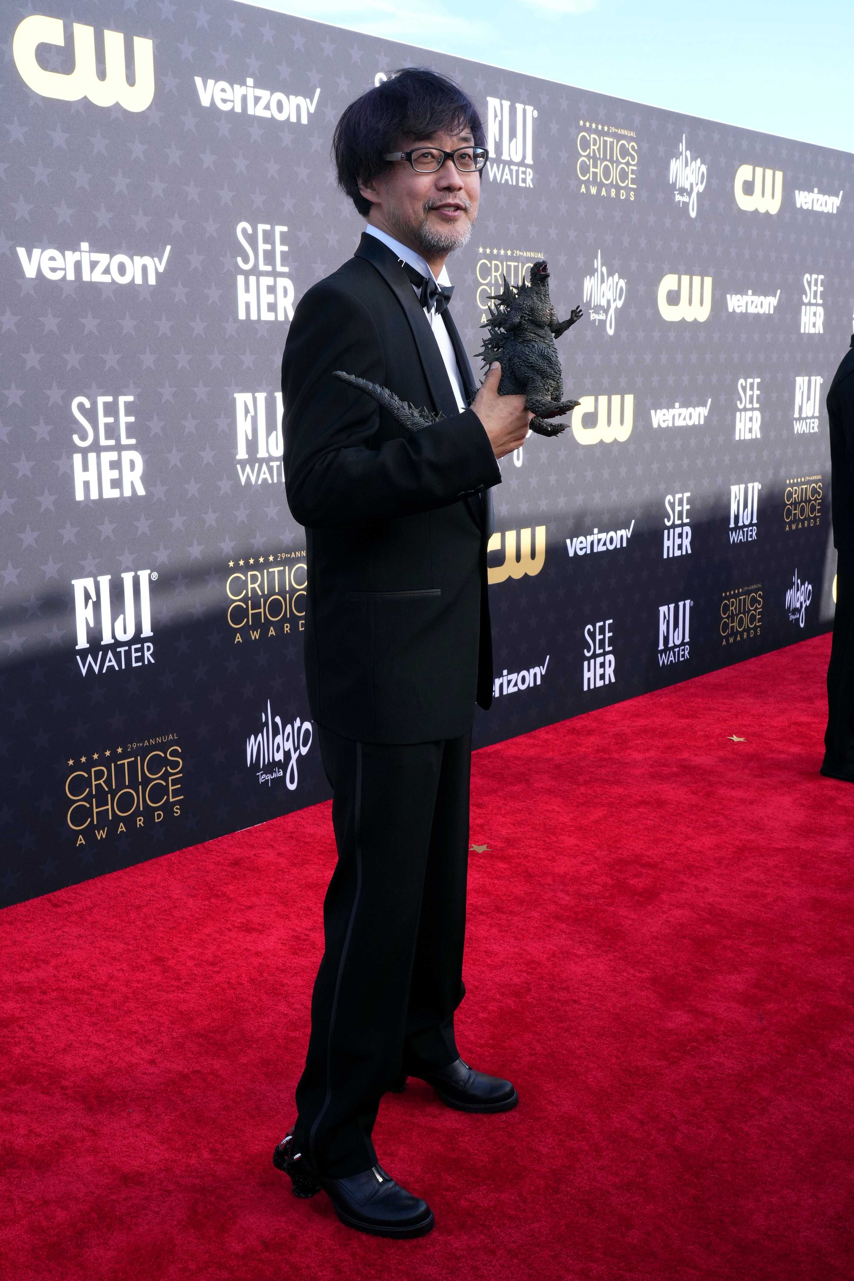 Takashi Yamazaki wearing a suit, holding a Godzilla figurine