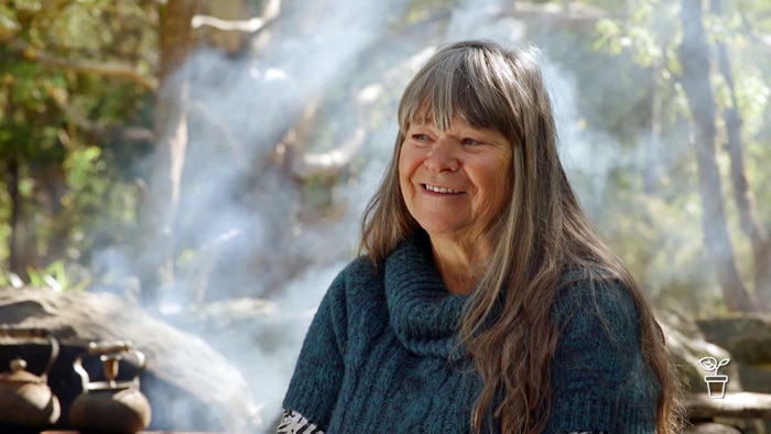 Woman smiling in outdoor bush setting with campfire smoke in the air