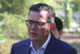 Premier Daniel Andrews stands under a tree in a reserve as he holds a press conference with journalists.