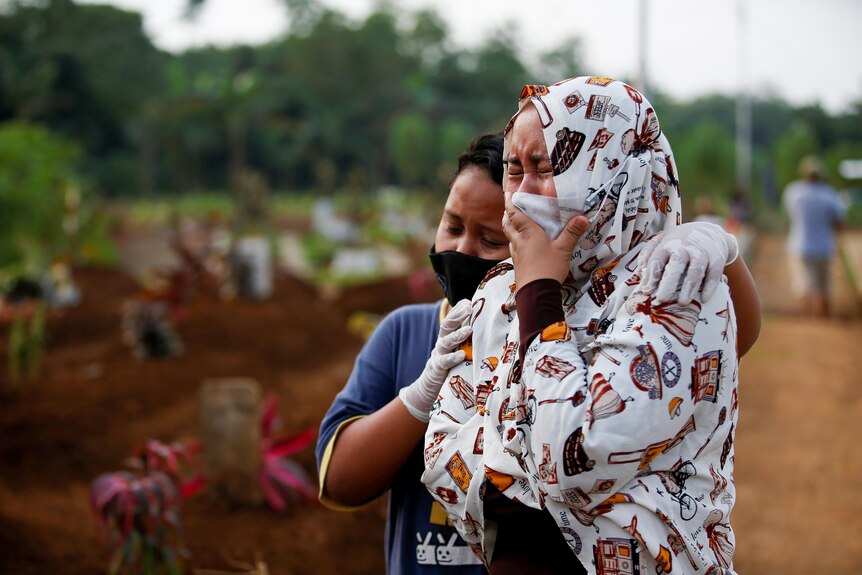 Two Indonesian women in face masks weep in 