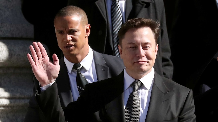 Wearing a black suit, Elon Musk waves as he walks on the steps of the courthouse.