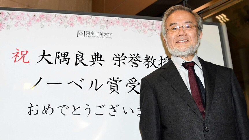 Yoshinori Ohsumi, a professor of Tokyo Institute of Technology smiles in front of a celebration message board.