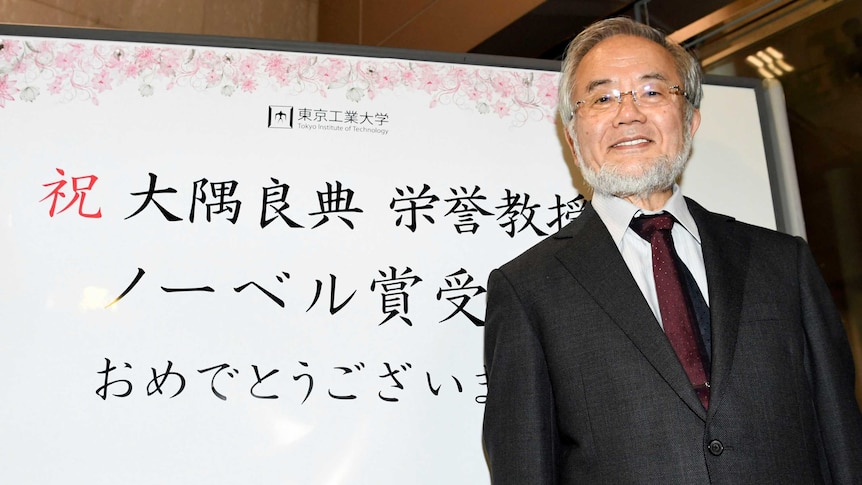 Yoshinori Ohsumi, a professor of Tokyo Institute of Technology smiles in front of a celebration message board.