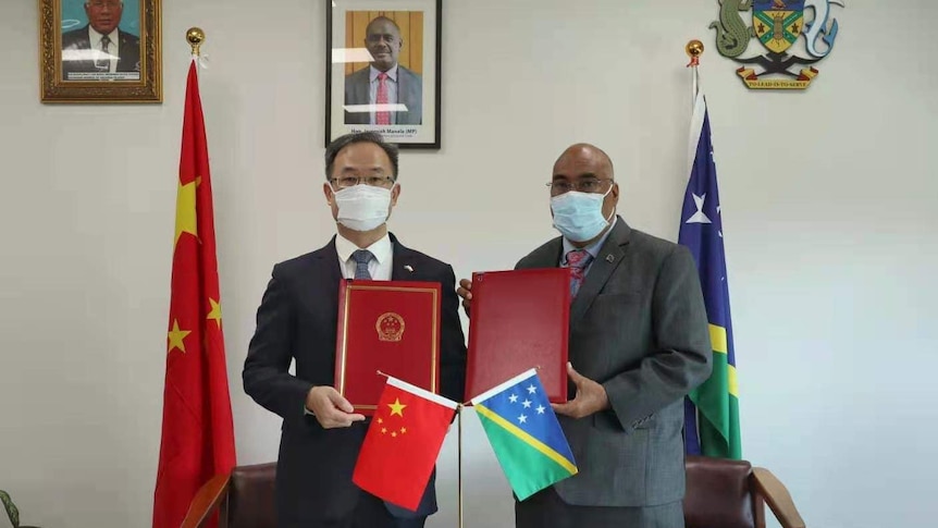 Li Meng and Colin Beck stand holding copies of a treaty. 