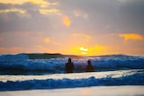 two people swimming at beach during sunrise