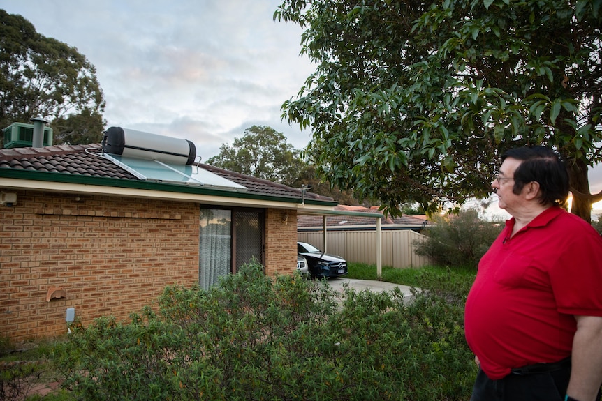 A man wearing a red polo shirt looks at a solar hot water system on his roof. 
