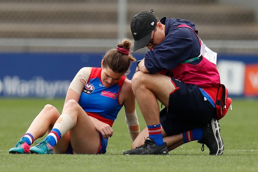 Kirsten McLeod is tended to by a trainer while she sits on the turf at Whitten Oval