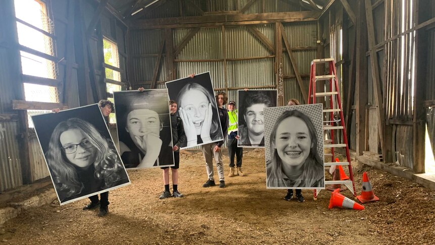 five students in a shed hold up giant A1 size black and white portrait photos of other students' faces
