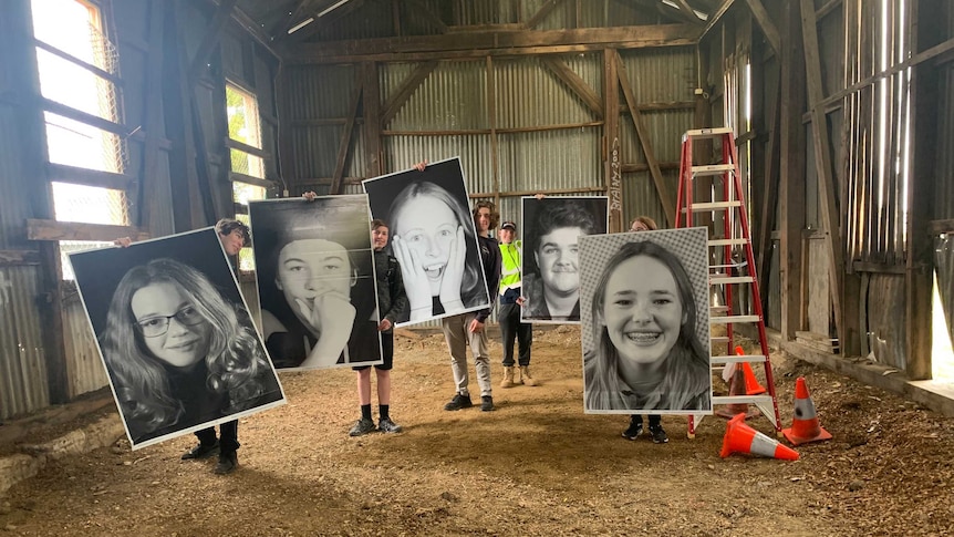 five students in a shed hold up giant A1 size black and white portrait photos of other students' faces