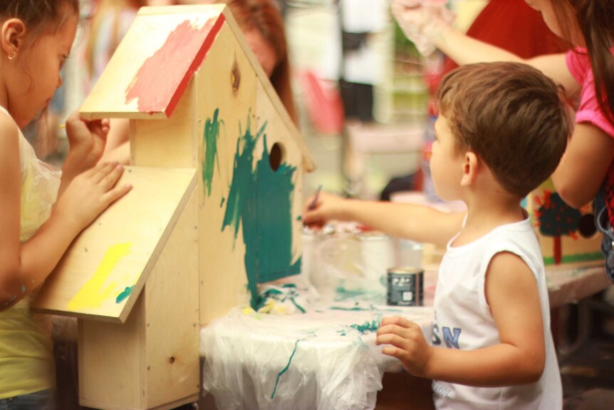 Children at daycare painting a little wooden house