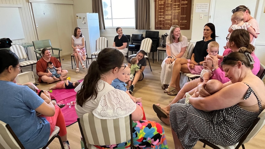 A group of women sitting on chairs in a circle holding babies in a room