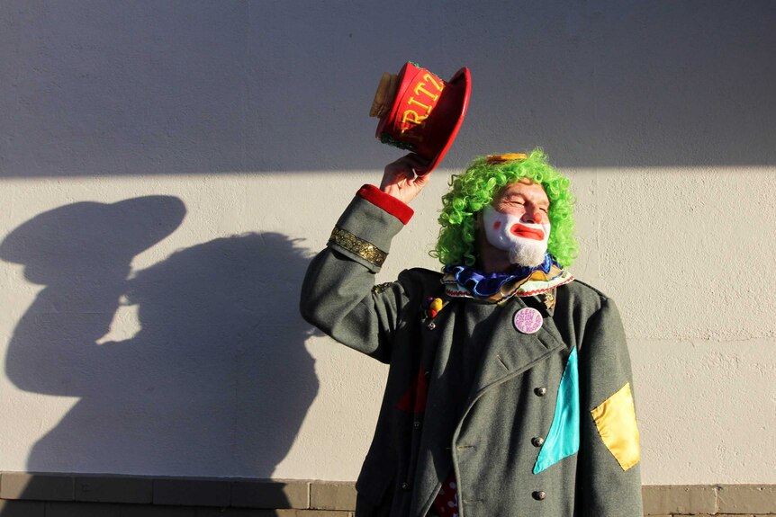 A brightly dressed clown tipping his top hat