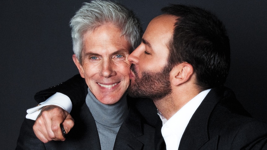 A man with short dark hair hugs and older man with grey white hair kissing his cheek