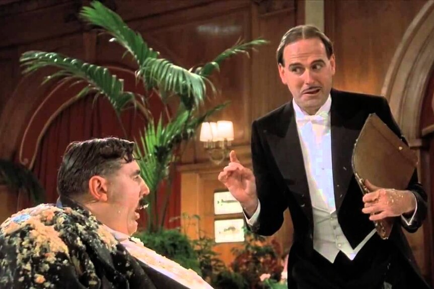 The maître d' (played by John Cleese) tempts Mr Creosote into ordering more food.