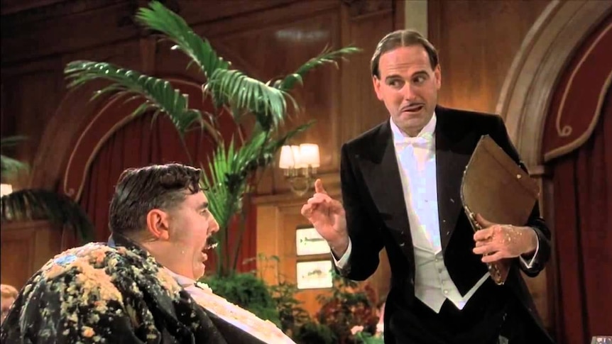 The maître d' (played by John Cleese) tempts Mr Creosote into ordering more food.