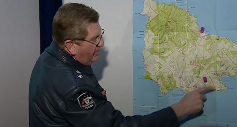 A male officer points at a map of Norfolk Island on the wall 