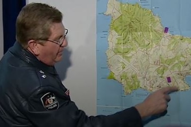 A male officer points at a map of Norfolk Island on the wall 