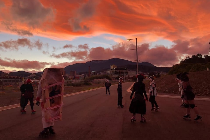Kids dressed up in Halloween costumes on roller skates with Mt Wellington and an orange sunset in the background.