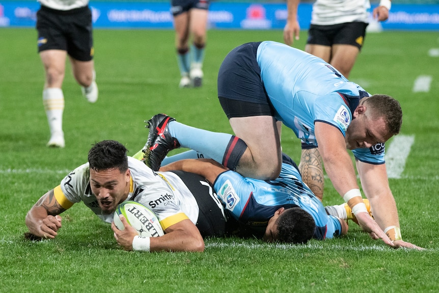 Rugby union player in the action of scoring a try with two opposition player attempting to tackle him