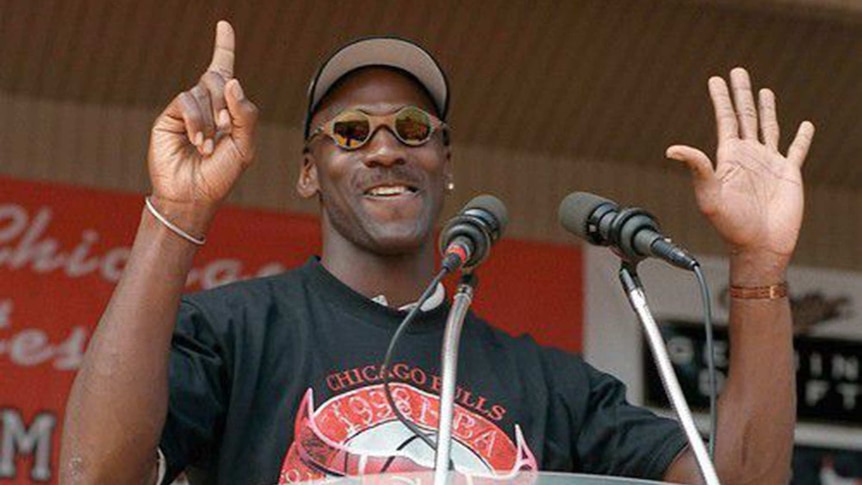 Michael Jordan holds up six fingers while standing at the podium at the Chicago Bulls' championship parade.