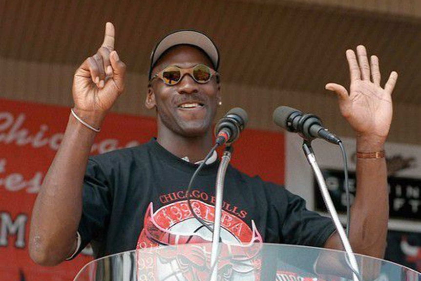 Michael Jordan holds up six fingers while standing at the podium at the Chicago Bulls' championship parade.