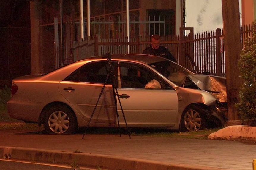 Police looking at a smashed up car on a pavement.