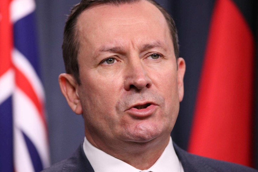 A tight head shot of WA Premier Mark McGowan speaking during a media conference indoors with flags behind him.