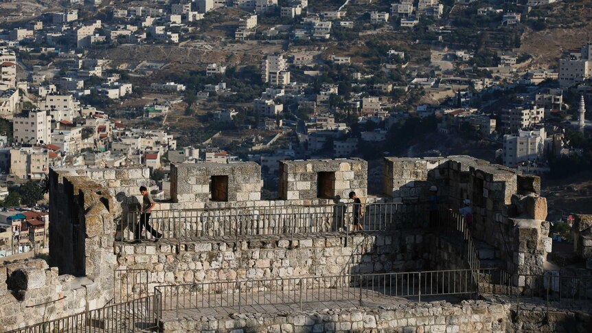 Arab neighbourhoods in East Jerusalem are seen in the background as children walk atop a wall surrounding Jerusalem's Old City