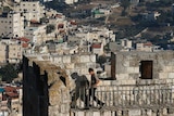 Arab neighbourhoods in East Jerusalem are seen in the background as children walk atop a wall surrounding Jerusalem's Old City