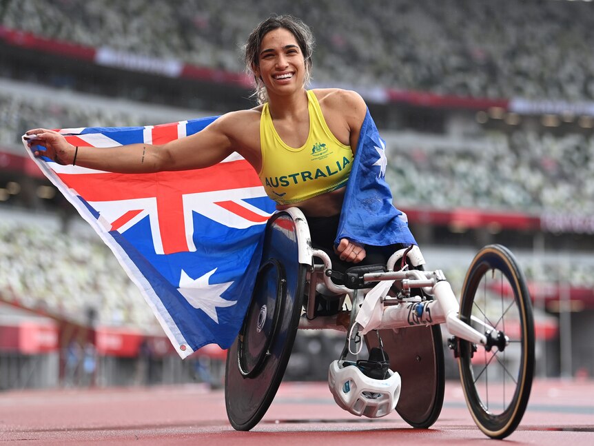 An Australian Paralympic athlete smiles as she sits in her wheelchair with an Australian flag wrapped around her.