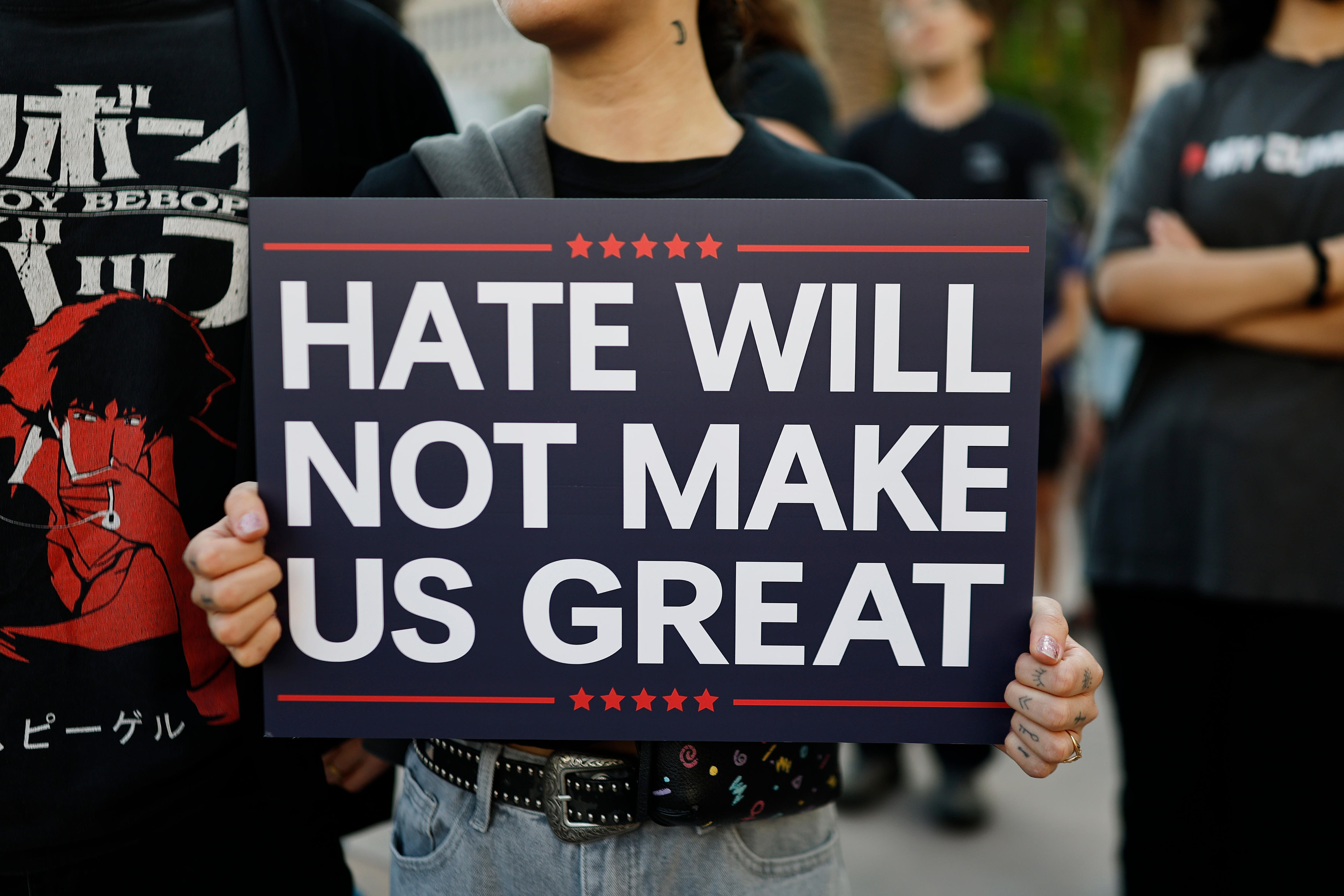 Hands holding a sign that reads "hate will not make us great".