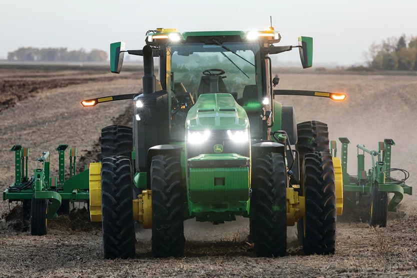 Tractor with no driver has lights on in field.