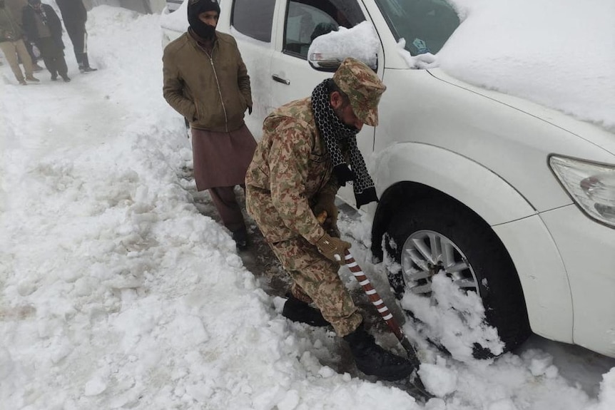 A soldier clears snow under a stranded vehicle.