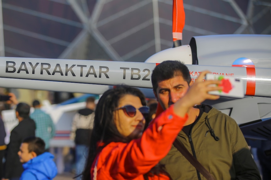 O femeie își face un selfie cu un bărbat în fața unui avion mic 