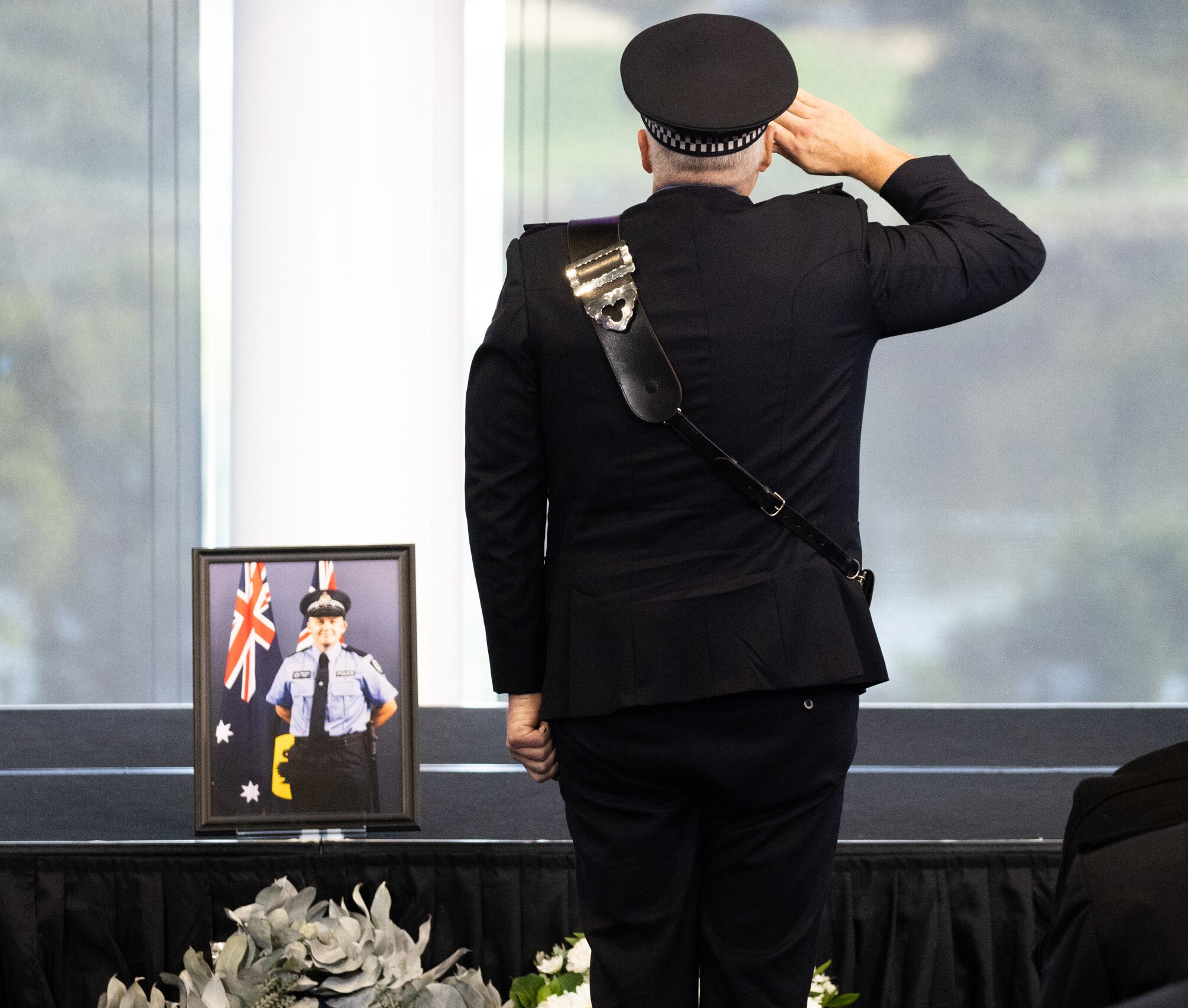 Police Commissioner Col Blanch salutes as he stands near Constable Woods's casket and photograph.