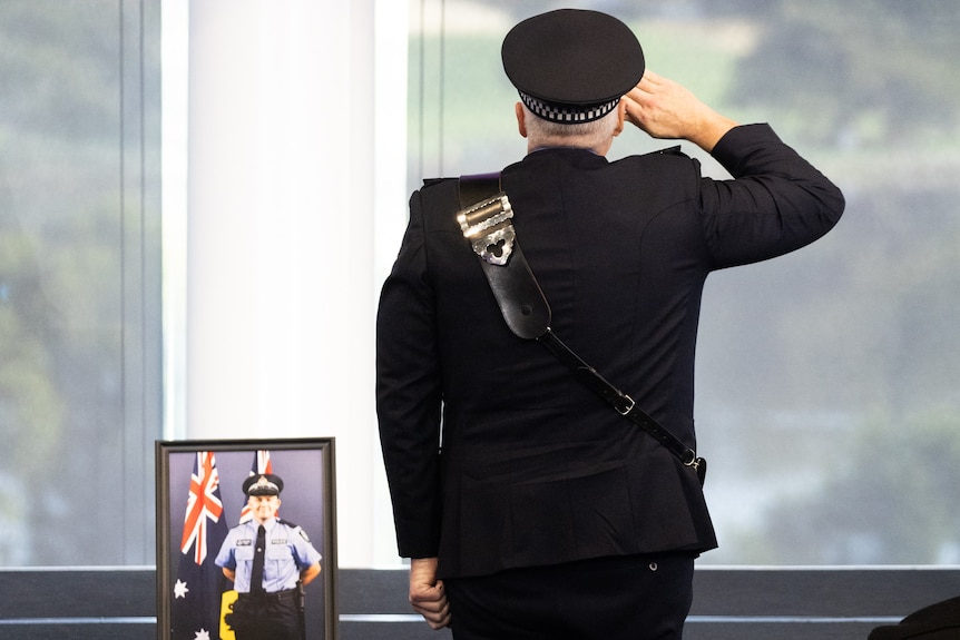 Police Commissioner Col Blanch salutes as he stands near Constable Woods's casket and photograph.