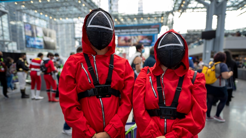 Two people dressed in red jumpsuits and black masks as Squid Game costumes