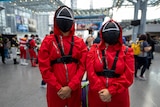 Two people dressed in red jumpsuits and black masks as Squid Game costumes