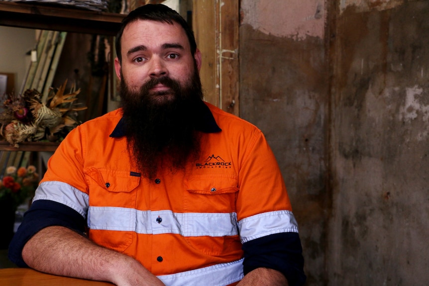 Portrait d'un homme barbu portant une chemise de travail boutonnée haute visibilité.