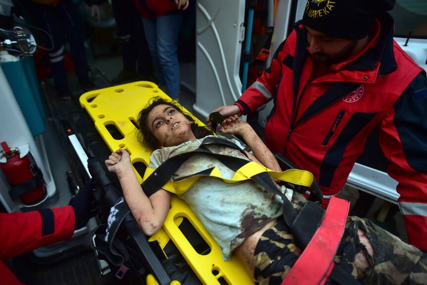 Young girl looks dazed as she lies on a stretcher after being rescued from under rubble.