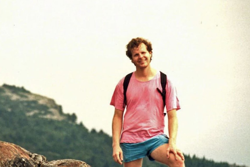 a man looking and smiling and standing on top of a cliff