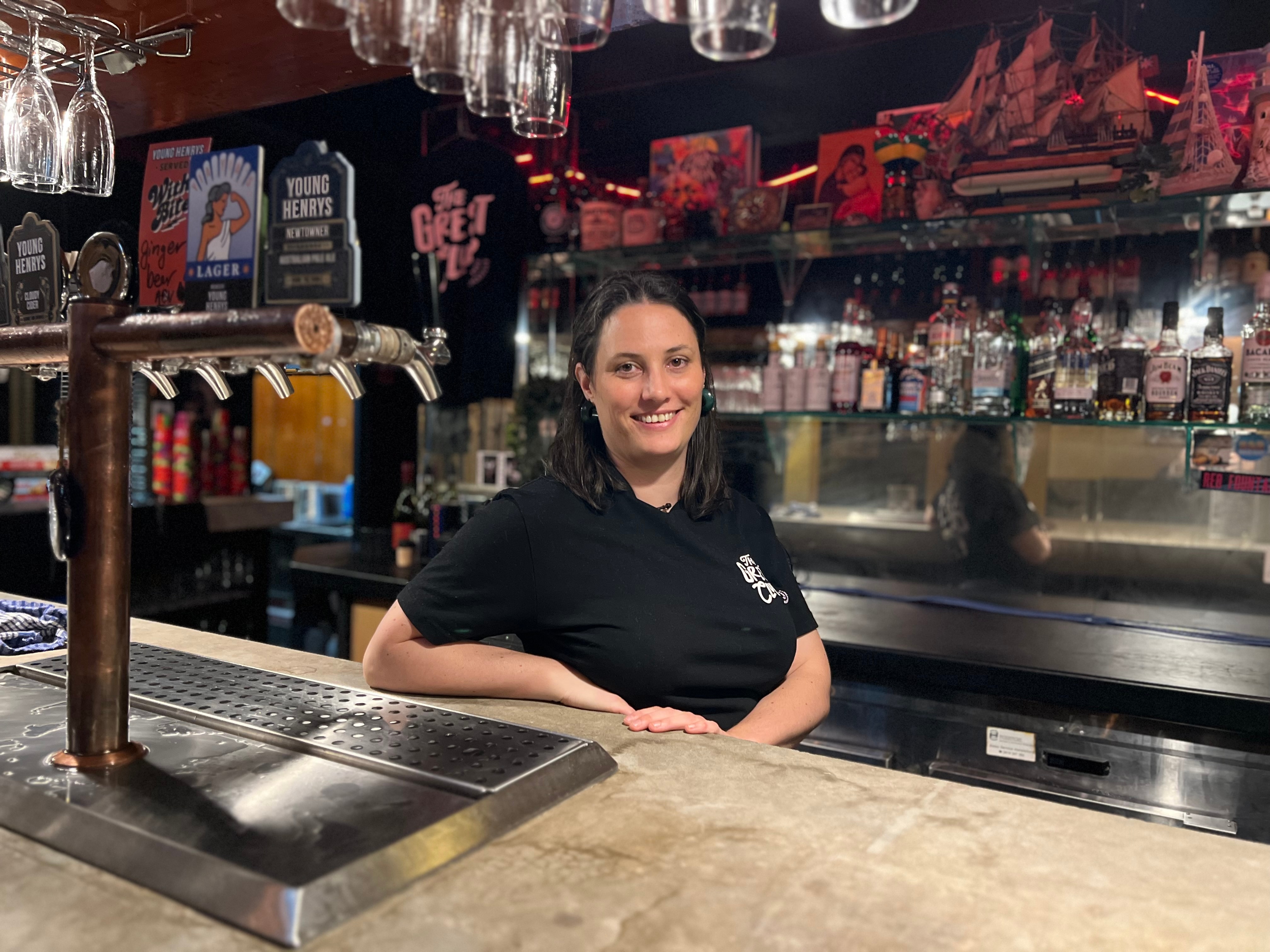 Alison Avron is wearing a black t-shirt as she leans on the bar behind beers taps in the great club marrickville