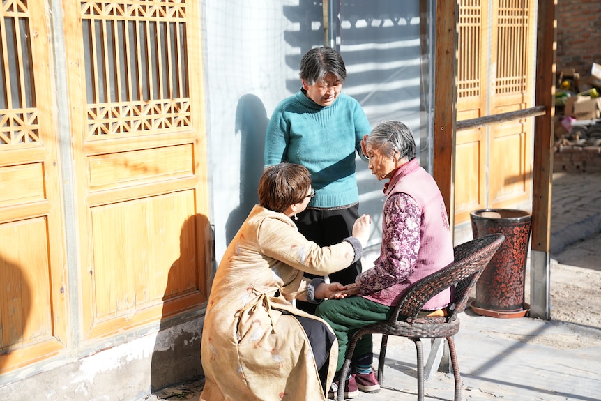 Two women talk to an elderly Chinese woman.