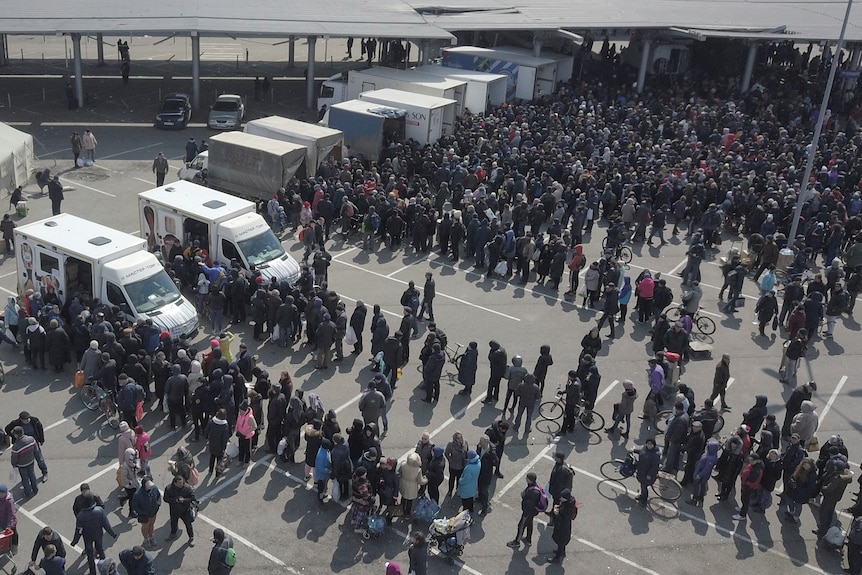 A drone photo of long lines of people lining up at numerous vans and shipping containers in a car park.
