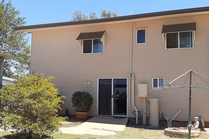 The back of a double-storey white brick home with a clothesline in the foreground